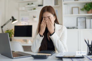 Stressed woman holding face in hands at desk, representing anxiety treatment and mental health support at Empower Health Group