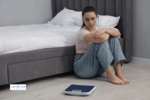 Young woman sitting on floor looking at scale, symbolizing bulimia nervosa treatment and eating disorder recovery at Empower Health Group
