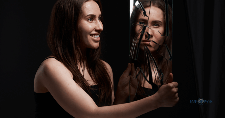Woman smiling while holding a cracked mirror showing her reflection, symbolizing bipolar disorder and addiction treatment at Empower Health Group