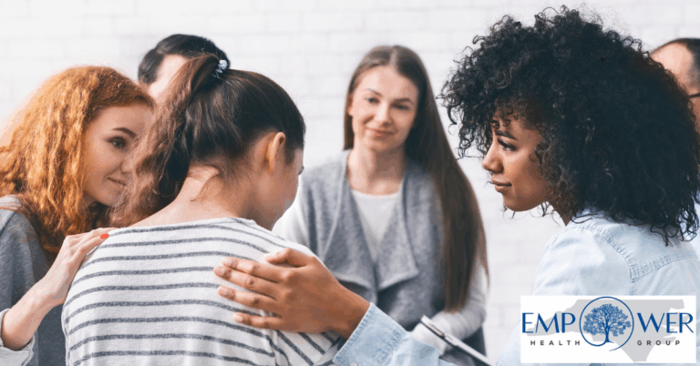 Support group offering comfort as several people encourage and console a distressed participant, with the Empower Health Group logo displayed.