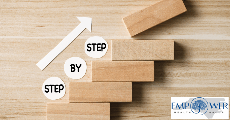 Wooden blocks arranged like ascending steps with the words “step by step” and an upward arrow, symbolizing progress, alongside the Empower Health Group logo.