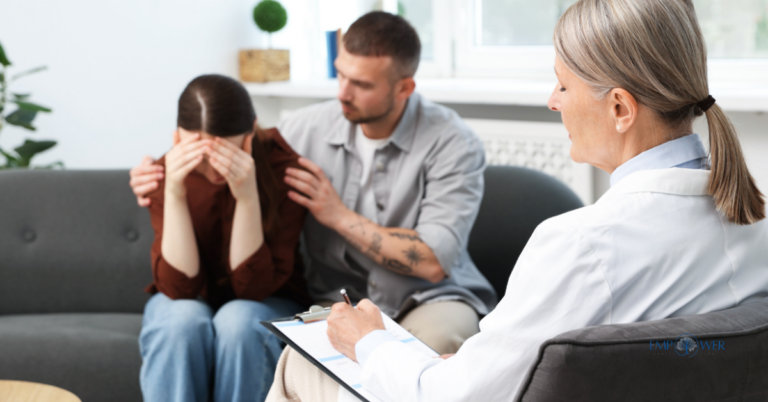 A female therapist taking notes while a man comforts a woman in distress on a sofa, representing the supportive environment of family therapy for addiction.