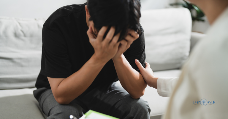 A person in a black shirt sitting on a sofa with their head in their hands, receiving a comforting hand on the arm during a complex PTSD treatment session.